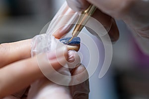 The master of the nail service makes a manicure by distributing gel polish on the surface of the nail with a thin nail brush