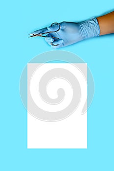 Master nails in blue gloves holds manicure scissors. sheet of white paper. manicure accessories on blue background top view.