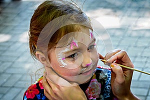 The master paints a beautiful figure on the face of a little girl with a brush. The child is impregnated with makeup in the form