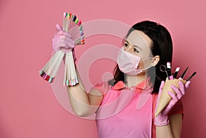 Master in pink gloves, apron and white mask holds manicure equipment in waffle cone and looks at nail varnish samples display