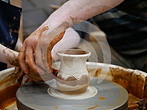 The master Potter helps the child to paint a clay jug with white paint on a modern Potter`s wheel with an electric drive.