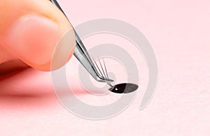 Master puts drop of glue on eyelash bundle extension procedure, pink background