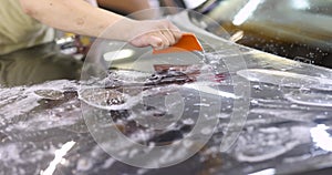 Master repairman glueing protective vinyl film on hood of car in garage 4k movie