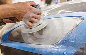 Master repairman polishing headlights of car in workshop using machine closeup.