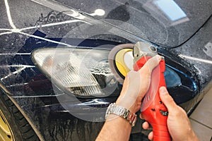 Master repairman polishing headlights of car in workshop using machine closeup.