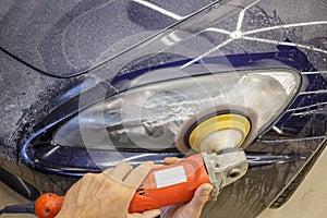 Master repairman polishing headlights of car in workshop using machine closeup.