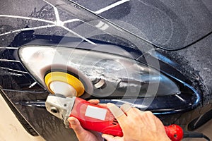 Master repairman polishing headlights of car in workshop using machine closeup.