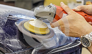 Master repairman polishing headlights of car in workshop using machine closeup.