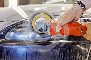 Master repairman polishing headlights of car in workshop using machine closeup.