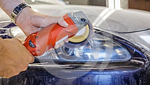 Master repairman polishing headlights of car in workshop using machine closeup.