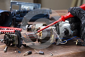 The master repairs a broken electrical device: drill, cutter on a wooden table. Electric Tool Repair Shop