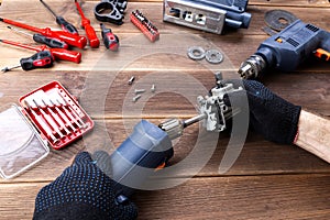 The master repairs a broken electrical device: drill, cutter on a wooden table. Electric Tool Repair Shop