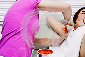 He master`s hands depilate the client`s armpits with wax, lather the colored wax with a wooden spatula photo