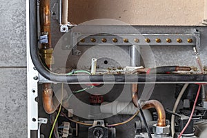 The master sets up a gas boiler, which weighs on the wall. The front dashboard is open. Due to improper maintenance, a lot of