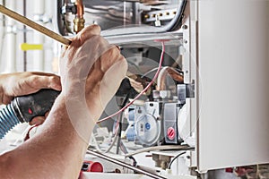 The master sets up a gas boiler, which weighs on the wall. The front dashboard is open. Using a brush and an industrial vacuum photo