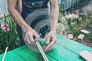 The master sharpens the wooden panel with an electric grinder on a Sunny day in the garden. Dimensioning