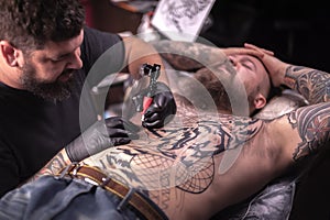 Master tattooist makes tattoo pictures in tattoo parlor