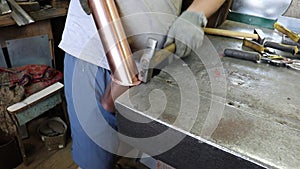 The master tinsmith knocks down the connecting lock on the copper pipe for the samovar by hand. Production.