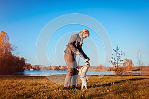 Master walking pug dog in autumn park by river. Happy woman feeding pet. Dog jumping to catch food