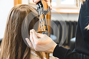 Master woman hairdresser gently curls hair curling girl in a beauty salon. Hair styling