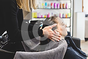 Master woman hairdresser gently washes the girl& x27;s hair with shampoo and conditioner before styling in a beauty salon.