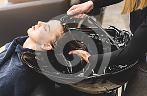 Master woman hairdresser gently washes the girl& x27;s hair with shampoo and conditioner before styling in a beauty salon.