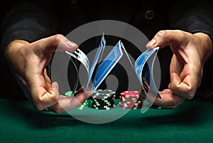 Masterly shuffling of playing cards with the hands of a dealer or croupier in a poker club on a green table with playing chips.