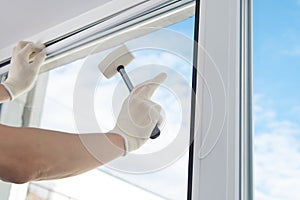 Masterâ€™s hand in protective gloves, fixes a double-glazed window with a plastic baseboard, hammering it with a rubber mallet,