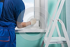 The masterâ€™s hands in white gloves adjust the installed plastic windows with a key to properly fit the window into the frame