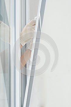 Masterâ€™s hands in white gloves install a mosquito net in a plastic window, closeup