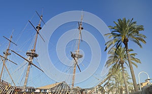 The masts of an ancient sailing ship with lowered sails in front of the blue sky and bright sunlight