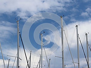 Masts of sailing yachts against the blue sky with white clouds. Yacht in the marina during the morning dawn sailing past the moore