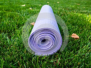 Mat for fitness lies on the green grass. Purple yoga Mat or Pilates