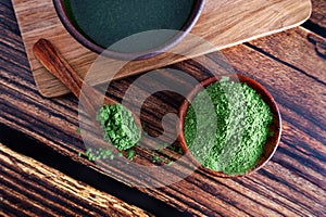 Matcha, chlorella or young barley grass in a bowl on a wooden background