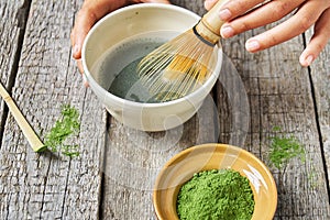 Matcha green tea accessoires on the rough wooden boards with girl`s hands preparing matcha tea in a clay bowl