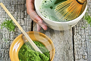 Matcha green tea accessoires on the rough wooden boards with girl`s hands preparing matcha tea in a clay bowl