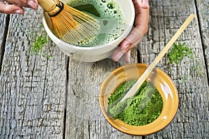 Matcha green tea accessoires on the rough wooden boards with girl`s hands preparing matcha tea in a clay bowl