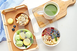 Matcha green tea, breakfast top view white background. oatmeal with berries, toasts on a wooden tray, nuts, coffee