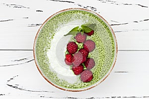 Matcha green tea chia seed pudding bowl, vegan dessert with raspberry and coconut milk. Overhead, top view, flat lay.