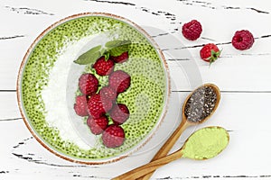 Matcha green tea chia seed pudding bowl, vegan dessert with raspberry and coconut milk. Overhead, top view, flat lay.