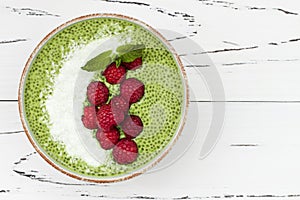 Matcha green tea chia seed pudding bowl, vegan dessert with raspberry and coconut milk. Overhead, top view, flat lay.