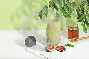 Matcha green tea latte in a glass with figs and honey on a modern light background with tropical leaves. Modern still life on a