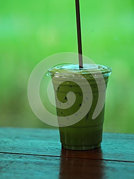 Matcha Green tea put milk ice in plastic glasses set on a wooden plate blurred of nature background