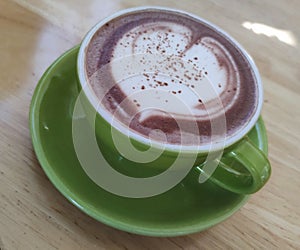 Matcha hot chocolate latte with heart shape of decoration soy coconut cow milk in green mug on wooden desk table at loft style c