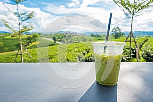 Matcha iced green tea in clear plastic glass on table with tea plantation background at Choui Fong Chiang Rai province, Thailand