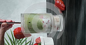 Matcha latte with strawberry, person tasting sweet milk cocktail, mixing with long spoon, green matcha, 4k vertical