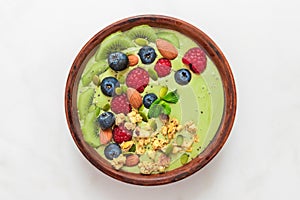 Matcha tea green smoothie bowl with fresh berries, nuts, seeds and homemade granola for healthy vegan diet breakfast