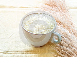 Matcha tea latte morning antioxidant hot drink in blue cup on yellow table cloth with pampas grass