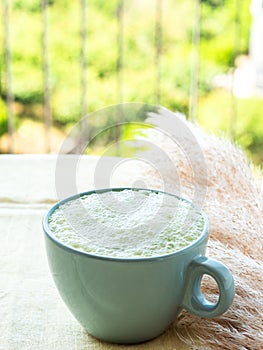 Matcha tea latte morning antioxidant hot drink in blue cup on yellow table cloth with pampas grass