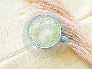 Matcha tea latte morning antioxidant hot drink in blue cup on yellow table cloth with pampas grass